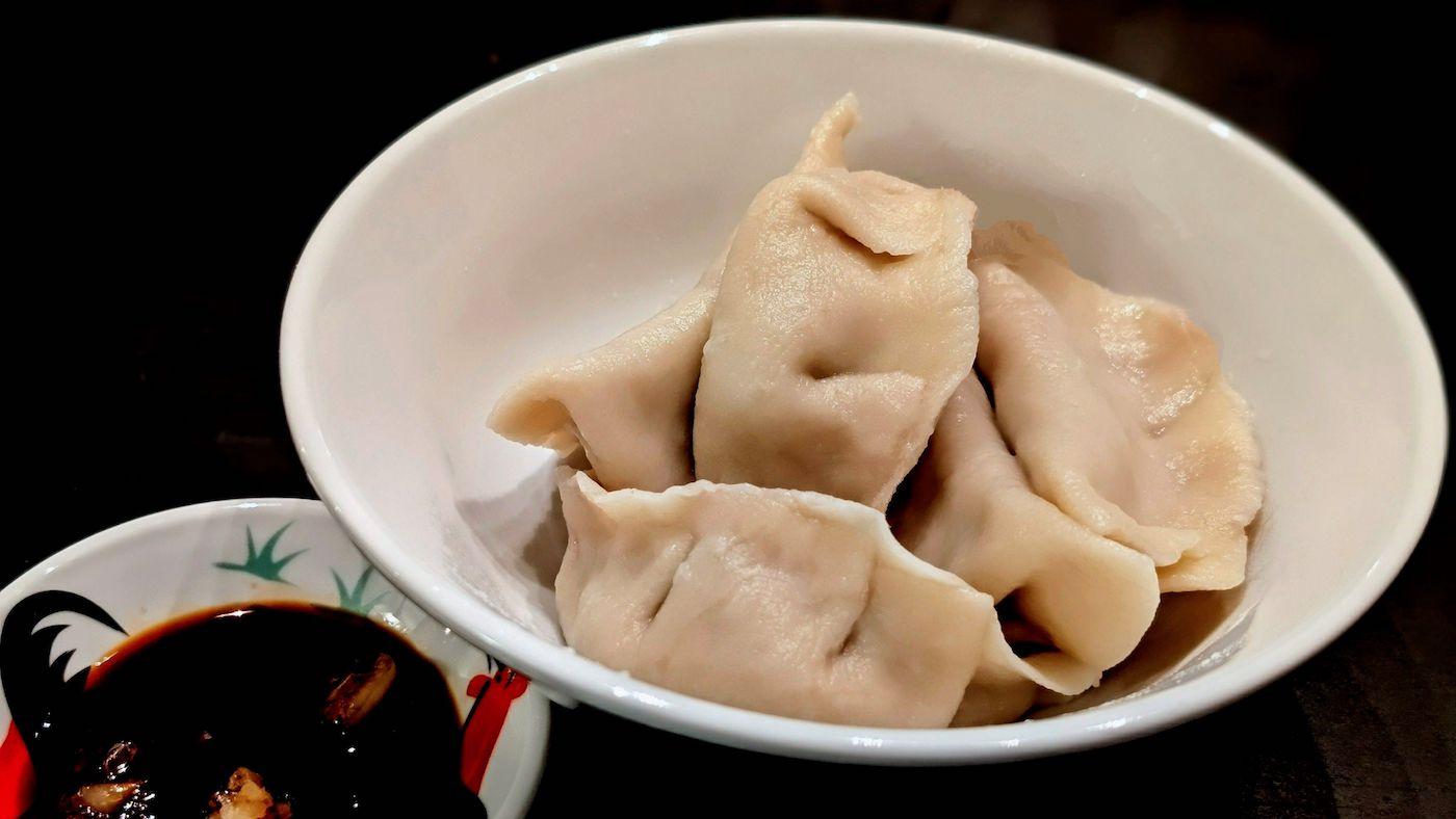Chinese dumplings in a white bowl next to a smaller bowl of dipping sauce