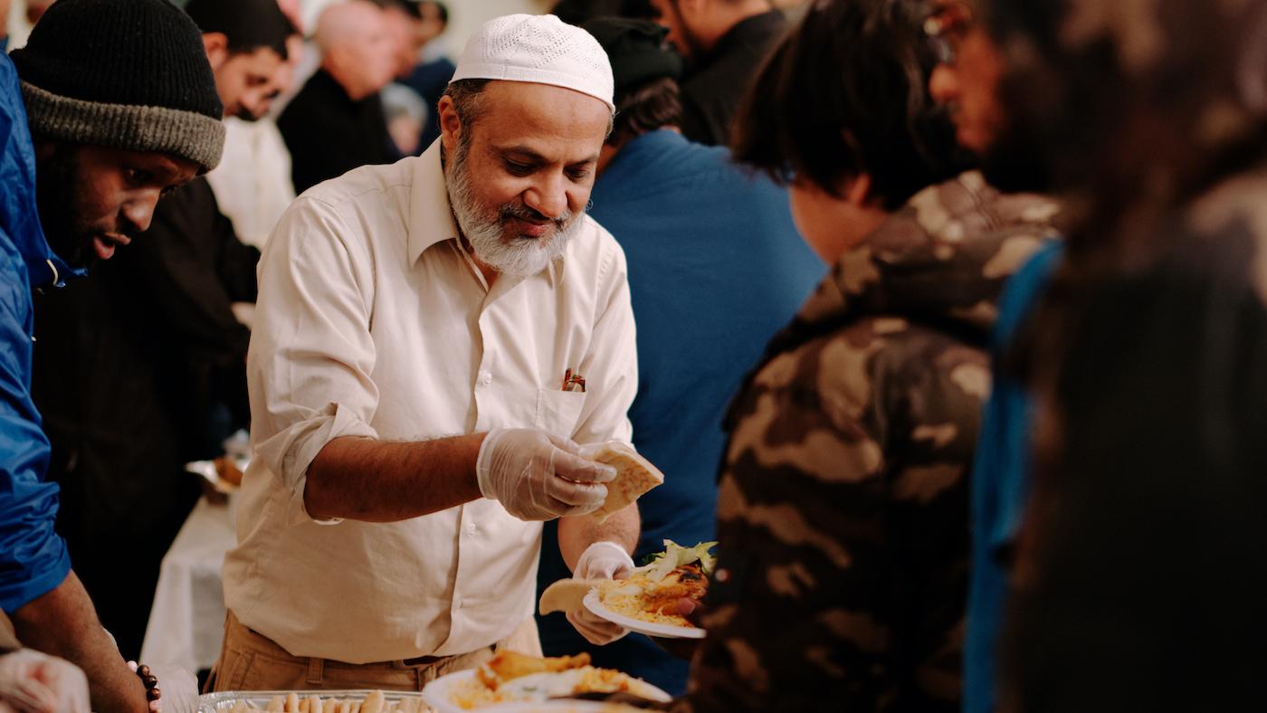 A man in plastic gloves puts pieces of pita on the plate of a person in line