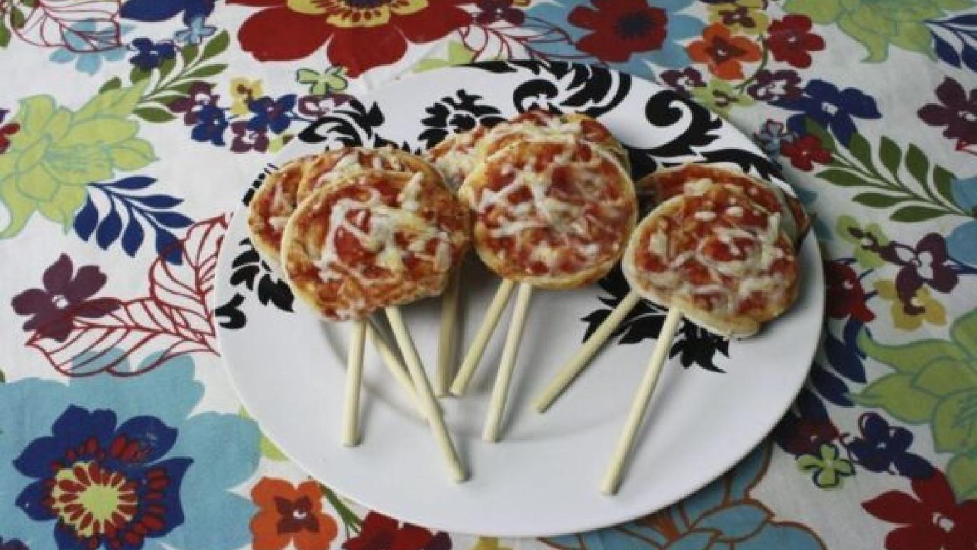A plate of mini pizzas on skewers on a flowered tablecloth