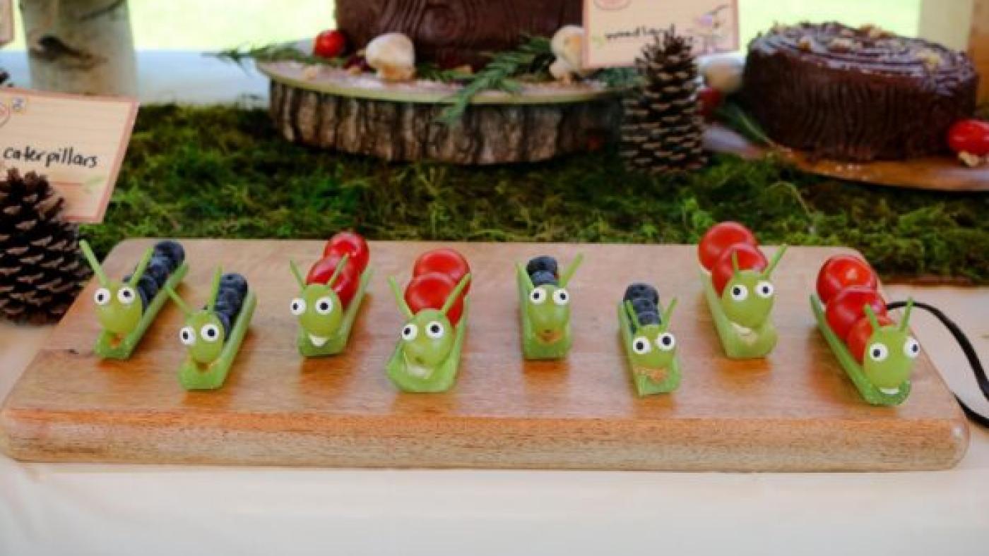 Snacks of fruit and celery that look like caterpillars on a board