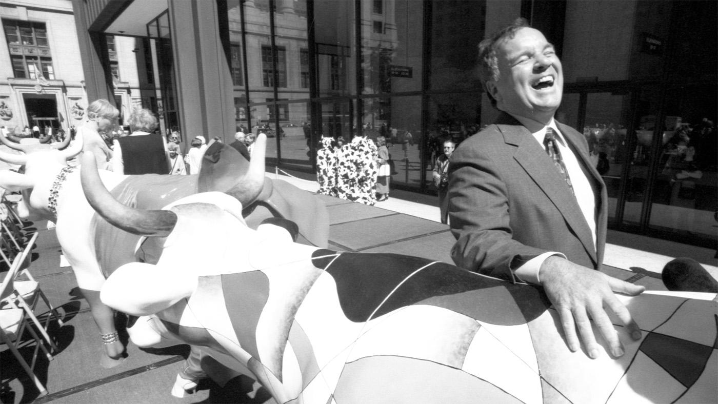 A black and white image of Mayor Richard M. Daley laughing with one of the Cows on Parade statue