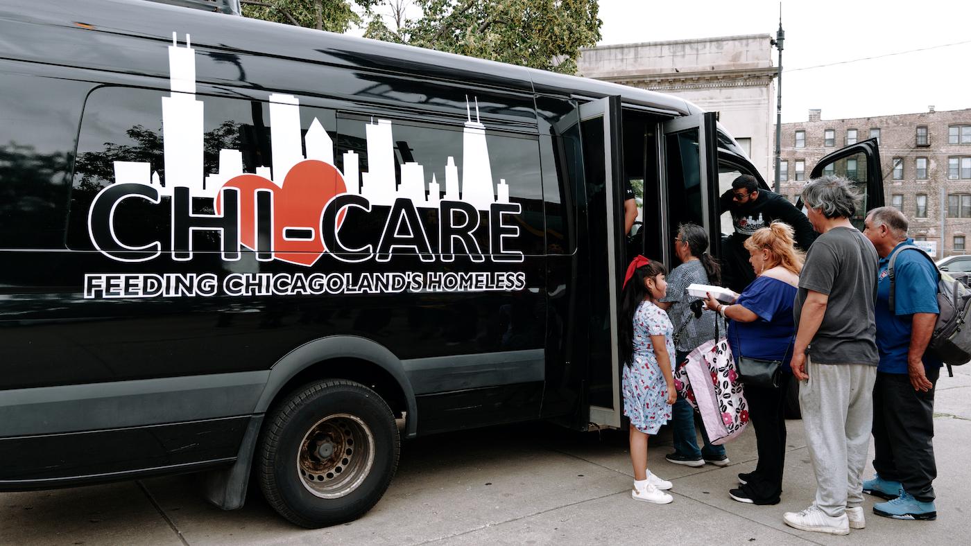People stand in line for food at the door of a black van with the logo for Chi-Care