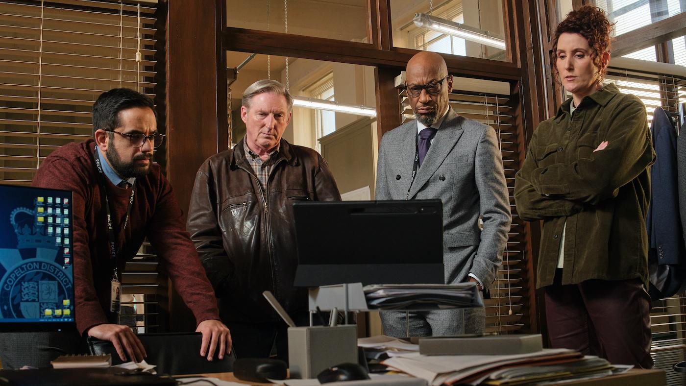 The team stands around a desk looking at a computer screen