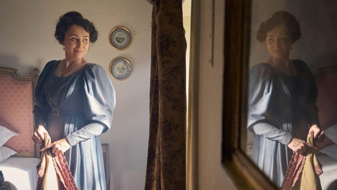 Keeley Hawes as Cassandra Austen smiles over her shoulder at herself in a mirror