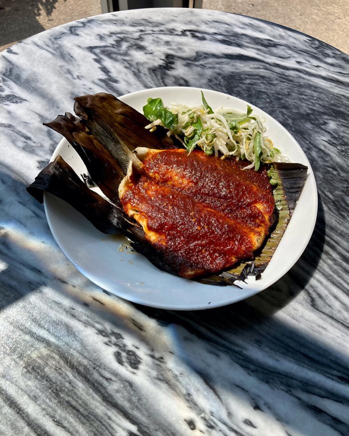 Ikan bakar (grilled fish) on a banana leaf with a side of kerabu (cucumber salad) on a table