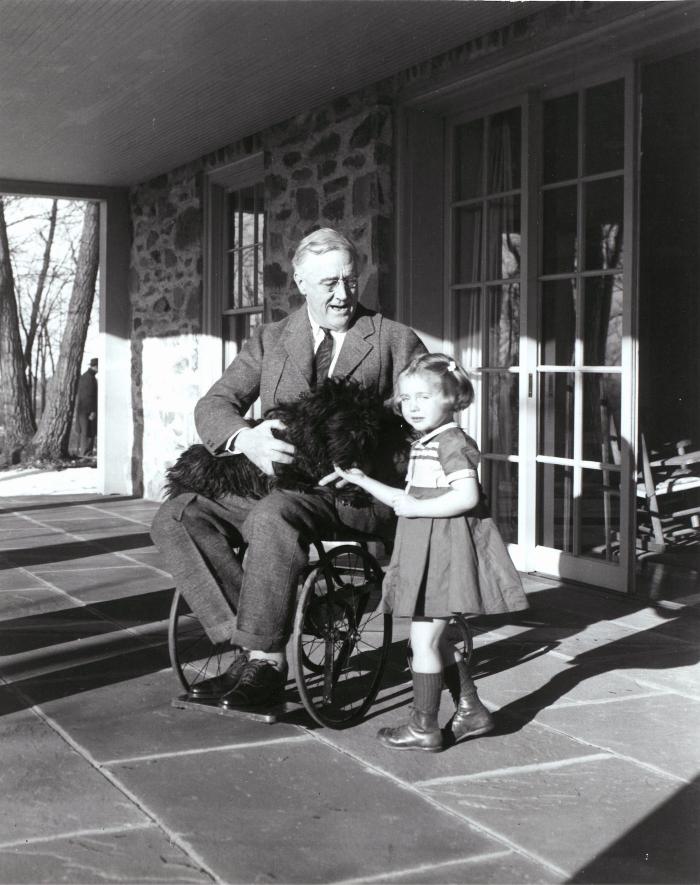 President Roosevelt in his wheelchair on the porch at Top Cottage in Hyde Park, NY with Ruthie Bie and Fala. February 1941. Photo: Margaret "Daisy" Suckley.; FDR Presidential Library and Museum 