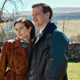 Helen and James stand next to each other in coats on a farm