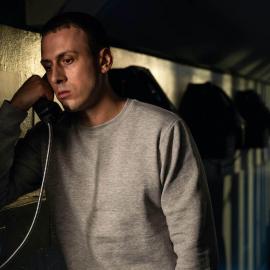 Jay Royce stands in shadows on a phone in prison