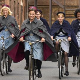 The midwives and their pupils ride bikes down the street, smiling in their uniforms 