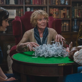Three women sit around a table that has shredded paper on it