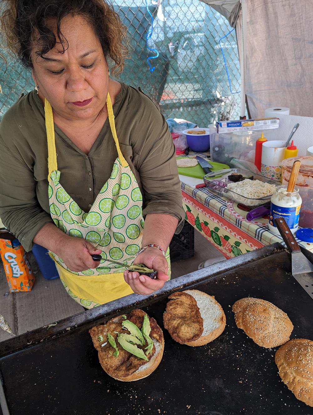 A woman adding sliced avocados to a cemita sandwich