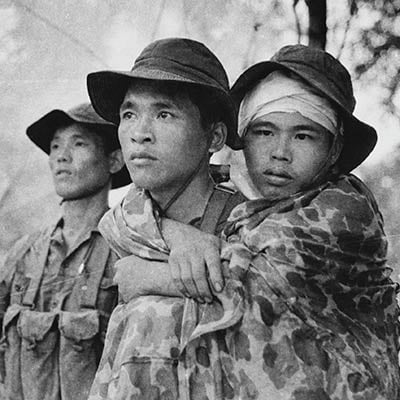 Viet Cong guerilla carries a wounded comrade, near the Cambodian border. Photo: Doug Niven